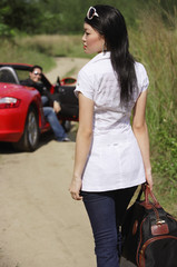Fototapeta na wymiar Woman with bag in foreground, man and red sports car in the background