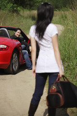 Woman standing on side of road, looking at man in red sports car