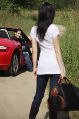 Naklejka premium Woman standing on side of road, looking at man in red sports car