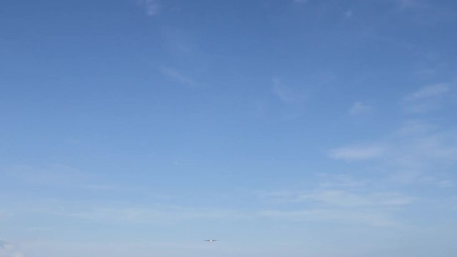 Airplane landing on island Bali airport. Cinematic shot of overhead flying aircraft on blue cloudy sky background. Enjoying happy summer vacation concept. Focal length 28mm