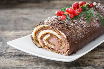 Chocolate yule log cake with red currant on wooden background
