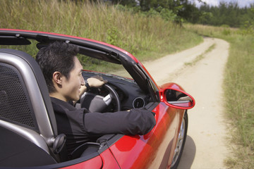 Fototapeta na wymiar Man driving red convertible sports car along country road