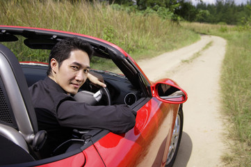 Man driving red convertible sports car, turning to look at camera