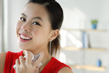 Young woman spraying perfume, smiling at camera