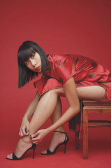 Woman in cheongsam, bending to adjust strap on shoes