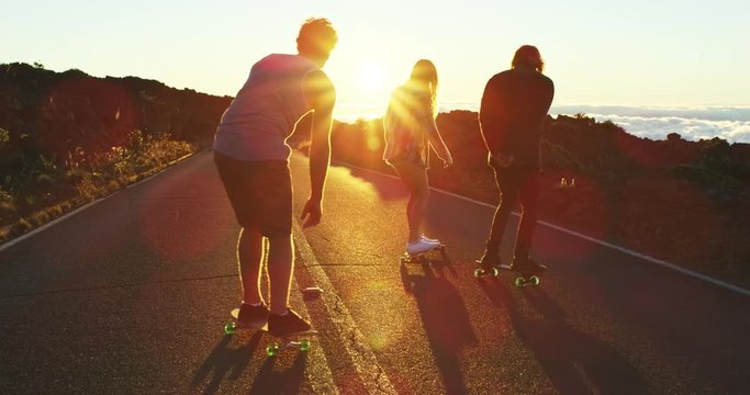 Skateboarders riding down mountain road into the sunset