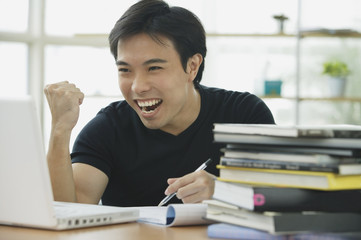 Young adult looking at laptop, smiling, making a fist