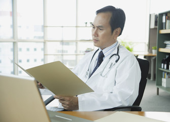 Doctor in office, looking at folder