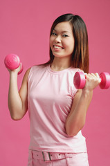 Woman dressed in pink, standing against pink wall, holding dumbbells