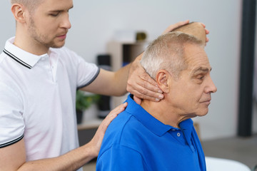 therapeut untersucht einen älteren mann am oberen rücken