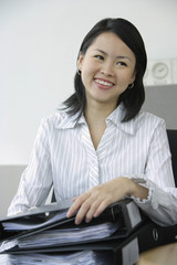 Young woman sitting at office desk, holding binders