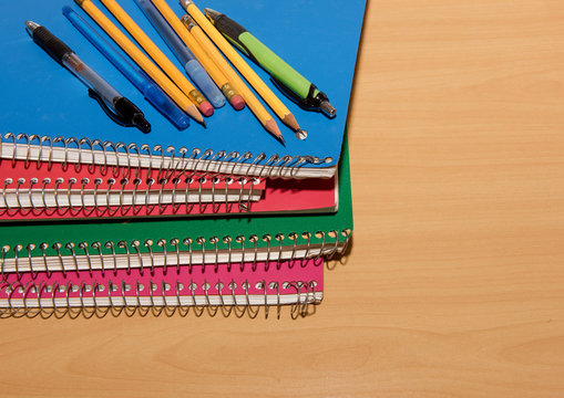 Stacked Notebooks With Pens And Pencils On A Wooden Desk