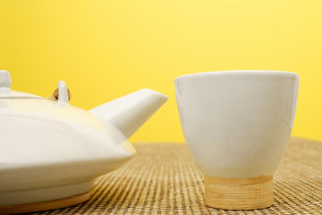 Still life with Chinese teacup and teapot, against yellow wall
