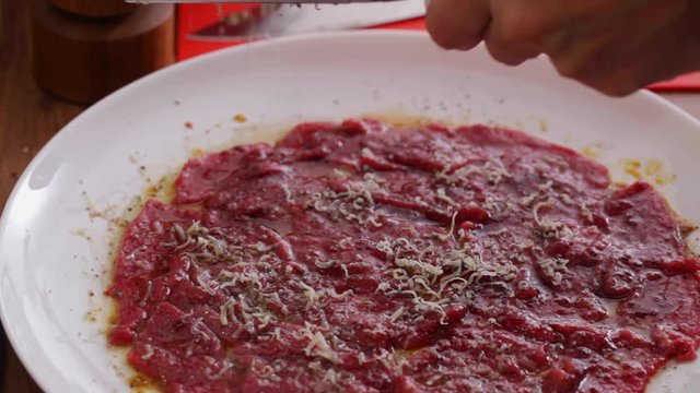 Chef grating hard cheese onto beef carpacio; close up; 