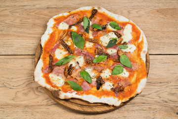 Homemade pizza with figs, prosciutto ham and mozzarella cheese on wooden serving board, top view