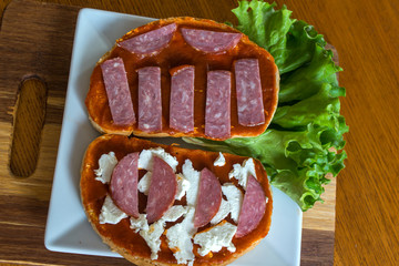 Slice of bread with chutney and feta cheese and salami on wooden background