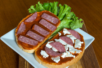 Slice of bread with chutney and feta cheese and salami on wooden background