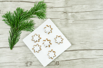Fototapeta na wymiar Kleiner quadratischer weißer Teller mit Weihnachtsplätzchen, Zimtsternen, einem Tannenzweig, Untergrund aus Holz, Textfreiraum