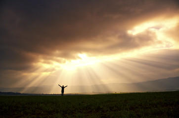 Young happy girl holding her arms up to the sky with dramatically spring sky and beautiful rays....