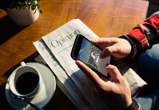 User with Smartphone, Newspaper, and Coffee Mockup 1
