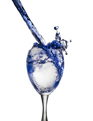 A blue drink is poured into wine glass causing a splash, isolated on white background