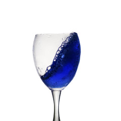 A blue drink is poured into wine glass causing a splash, isolated on white background