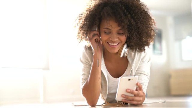 Smiling mixed-race girl laying on floor at home and using phone