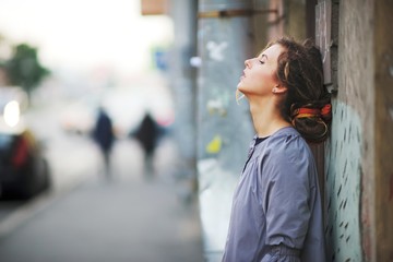 Sweetheart graceful girl in coat posing on a city street near the wall of the house, side view closeup.