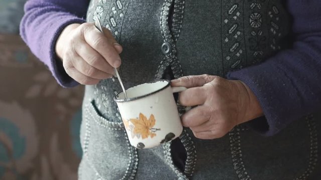Old woman's shaked hands stiring liquid in the metal mug
