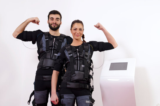 Happy man and woman next to EMS machine, muscle stimulation, showing muscles