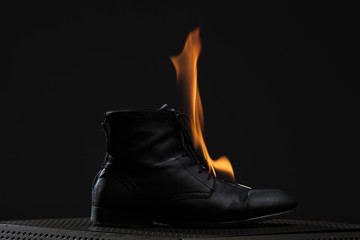Black leather boot burning on metal construction over black background