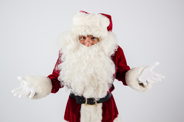 Santa Claus in eyeglasses and red costume throwing up hands on white background and looking into camera. American shot
