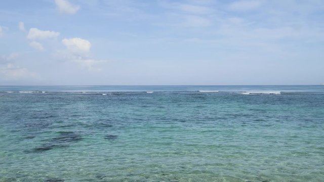 Airplane landing on island Bali airport under blue sea with waves on the horizon. Cinematic shot of overhead flying aircraft with beautiful ocean on cloudy sky background. Focal length 28mm