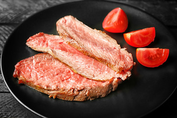 Black plate with delicious sliced steak on grey wooden background