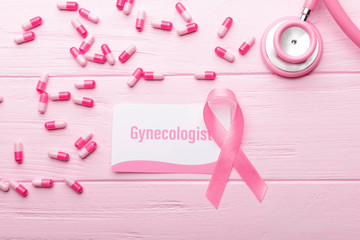 Business card with word GYNECOLOGIST, ribbon and pills on pink wooden background