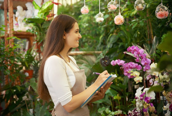 Pretty young florist with notebook and pen in greenhouse
