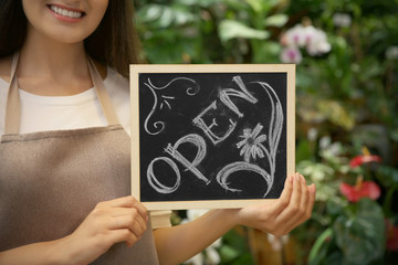 Young florist holding board with inscription OPEN, close up view