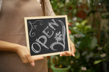 Young florist holding board with inscription OPEN, close up view