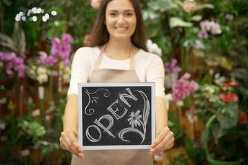 Pretty young florist holding board with inscription OPEN
