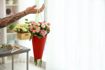 Hand of tattooed florist holding paper cone with beautiful bouquet, on blurred background