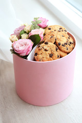 Box with beautiful flowers and cookies on light wooden background