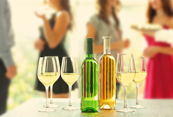 Bottles and glasses of white wine on table against blurred party background