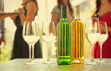 Bottles and glasses of white wine on table against blurred party background