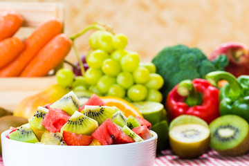 Fruit salad in a white bowl with vegetables background