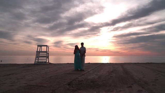 Pregnant couple talking at sunset. Love concept. Romantic couple on sea beach at sunset. Couple in love on sunset beach. Family on sea coast. Couple on sea beach. Love couple at sea beach at sunset