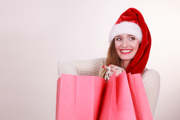 Christmas time. Young latin woman wearing santa claus hat holding red shopping bags buying presents gifts