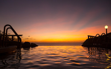 Infinity edge pool with sea underneath sunset