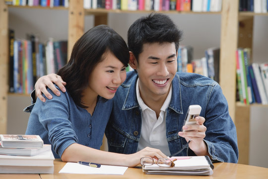 Couple in library, looking at mobile phone