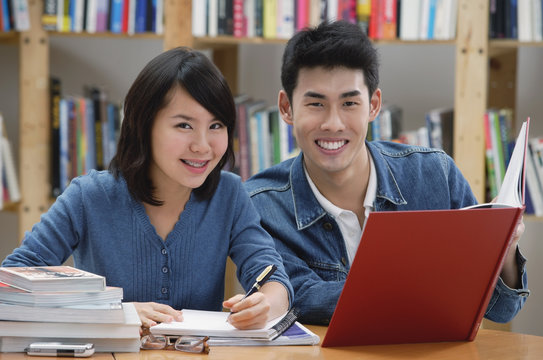 Couple studying in library, smiling at camera