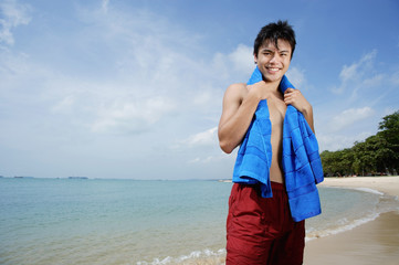 Man standing on beach, holding towel around his neck